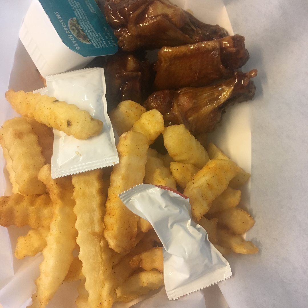 Wings, fries, and dipping sauces in a white container.