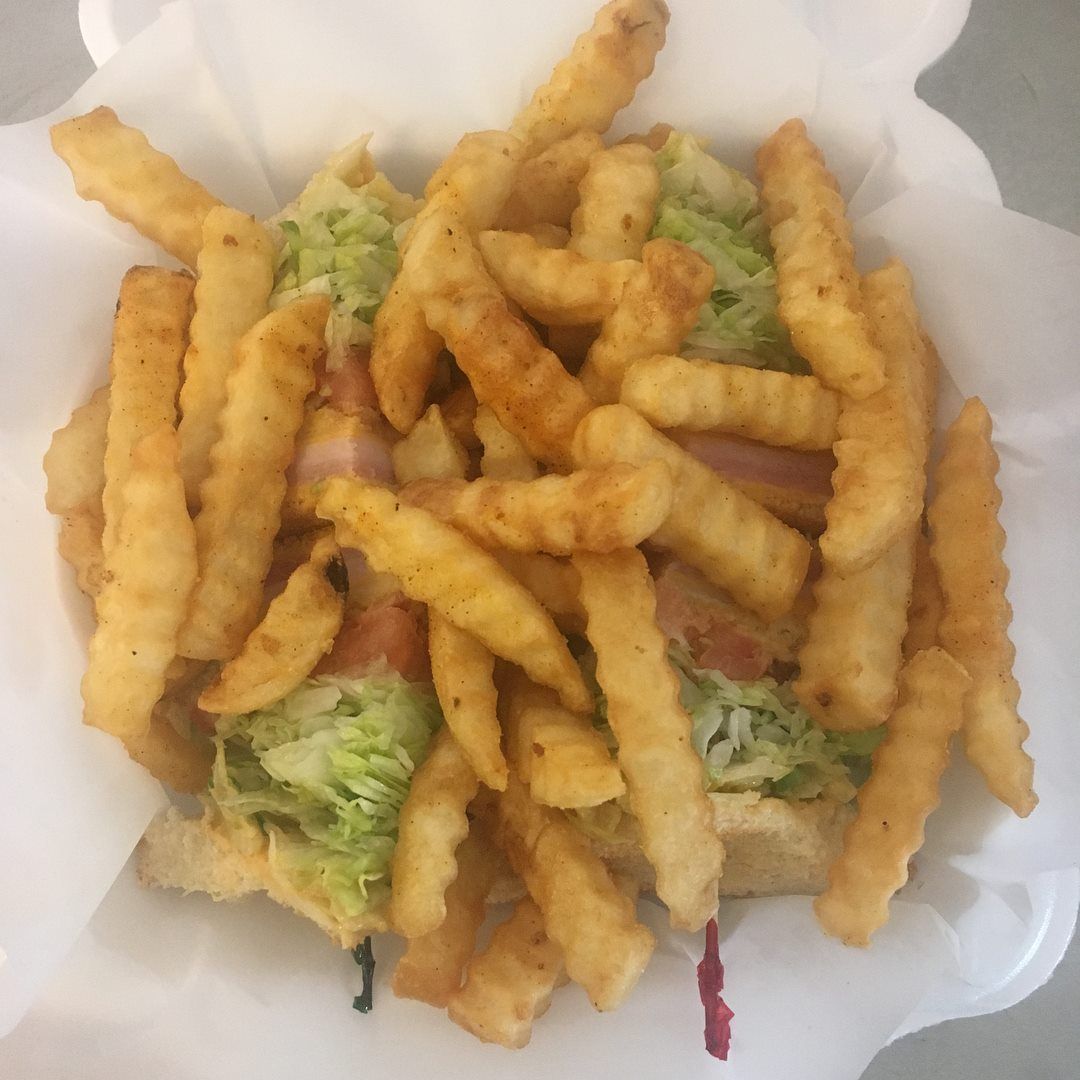 Sub sandwich with lettuce, bacon, and fries, in a white to-go container.