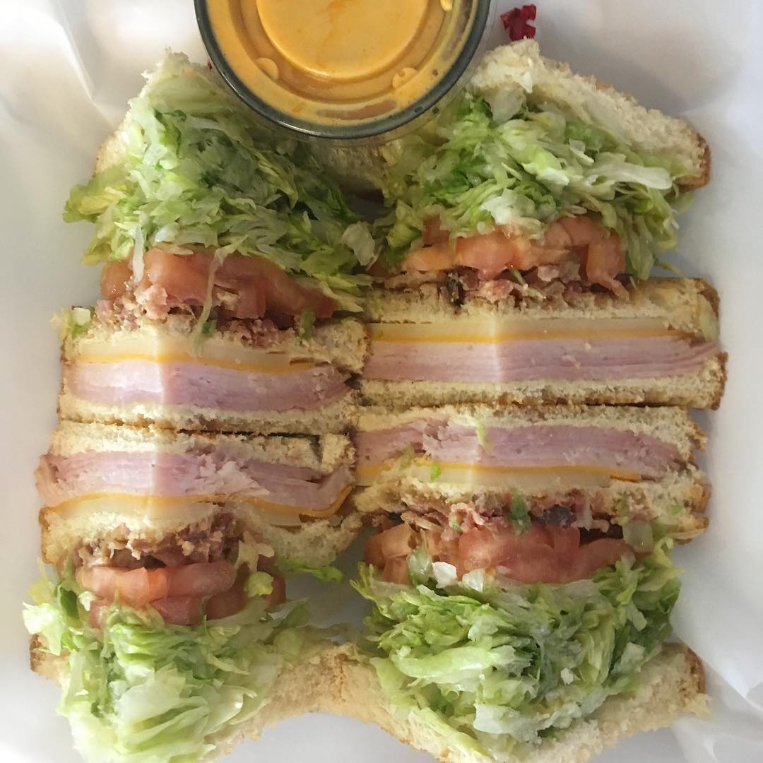 Club sandwich with ham, cheese, tomato, lettuce, and a dipping sauce.