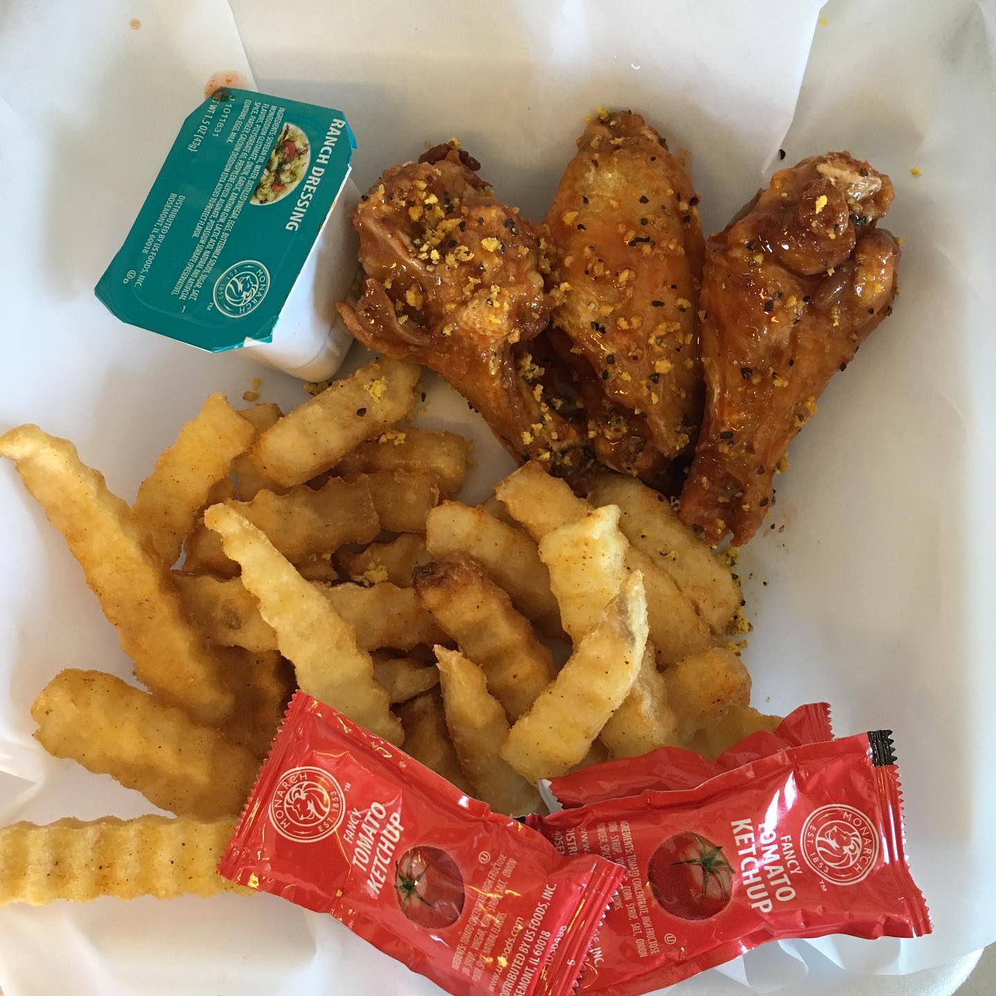 Chicken wings with fries, ketchup, and sauce in a takeout container.