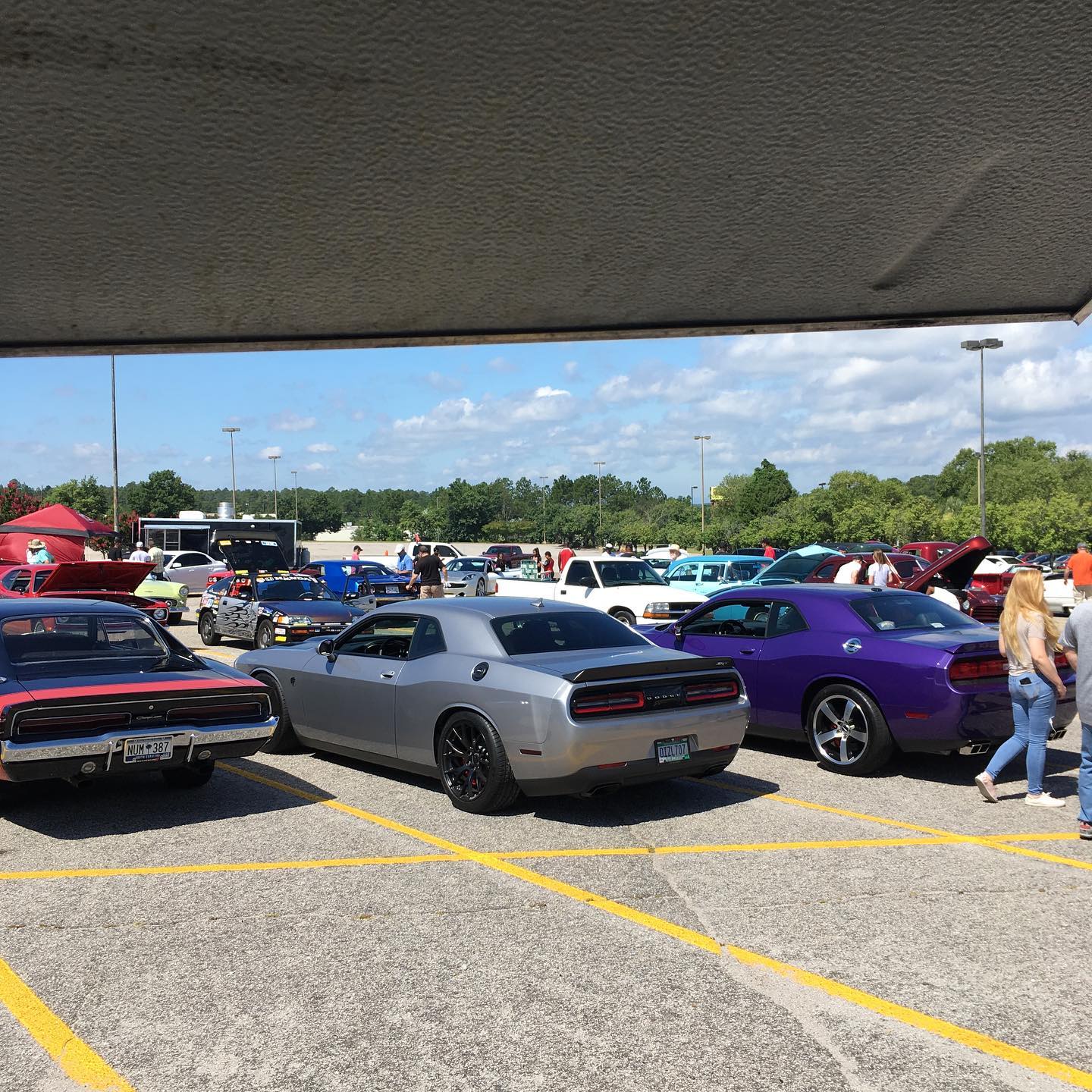 Cars parked in an outdoor car show on a sunny day, including silver, purple, and red vehicles.