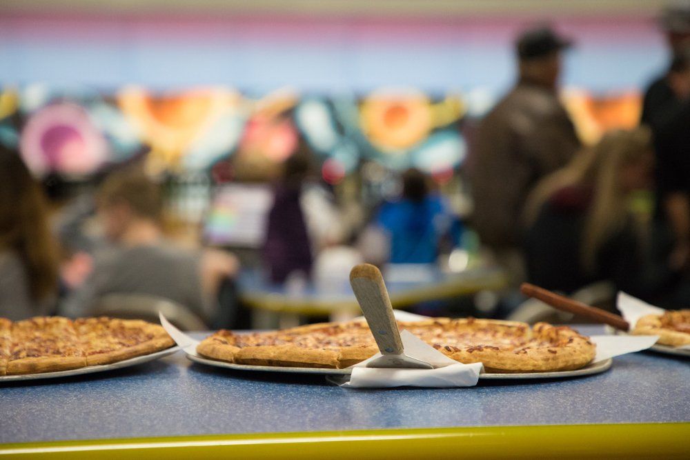 Pizzas on a table in a bowling alley, with people in the background.