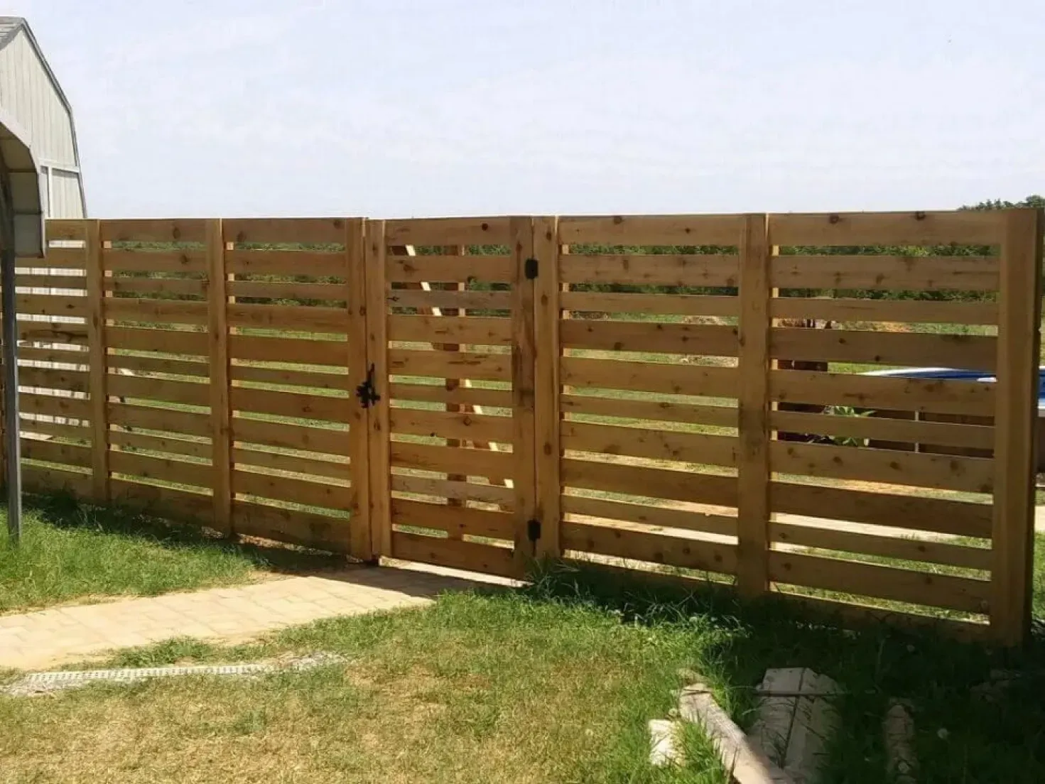 Wooden horizontal slat fence with gate, enclosing a grassy yard.