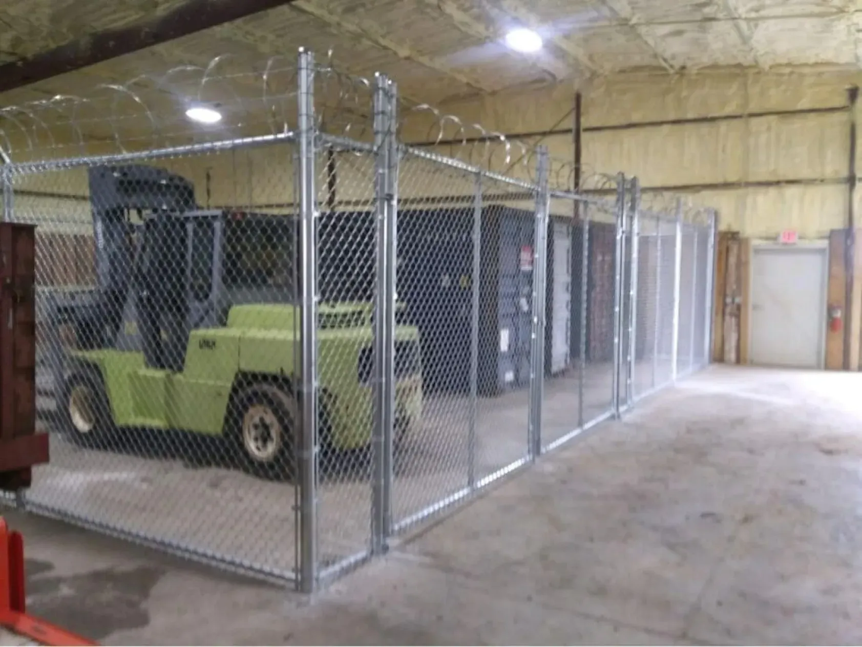 A forklift is parked in a warehouse behind a chain link fence.