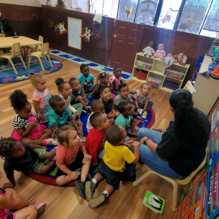 A woman sits in a chair reading a book to a group of children