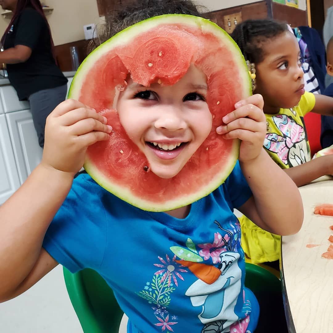 A little boy is holding a slice of watermelon in front of his face