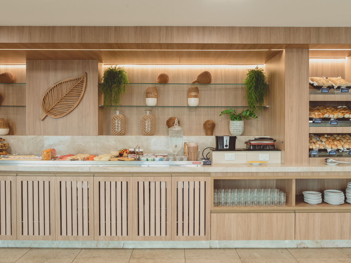 Buffet de café da manhã com armários de madeira, prateleiras de vidro e diversos itens alimentares.