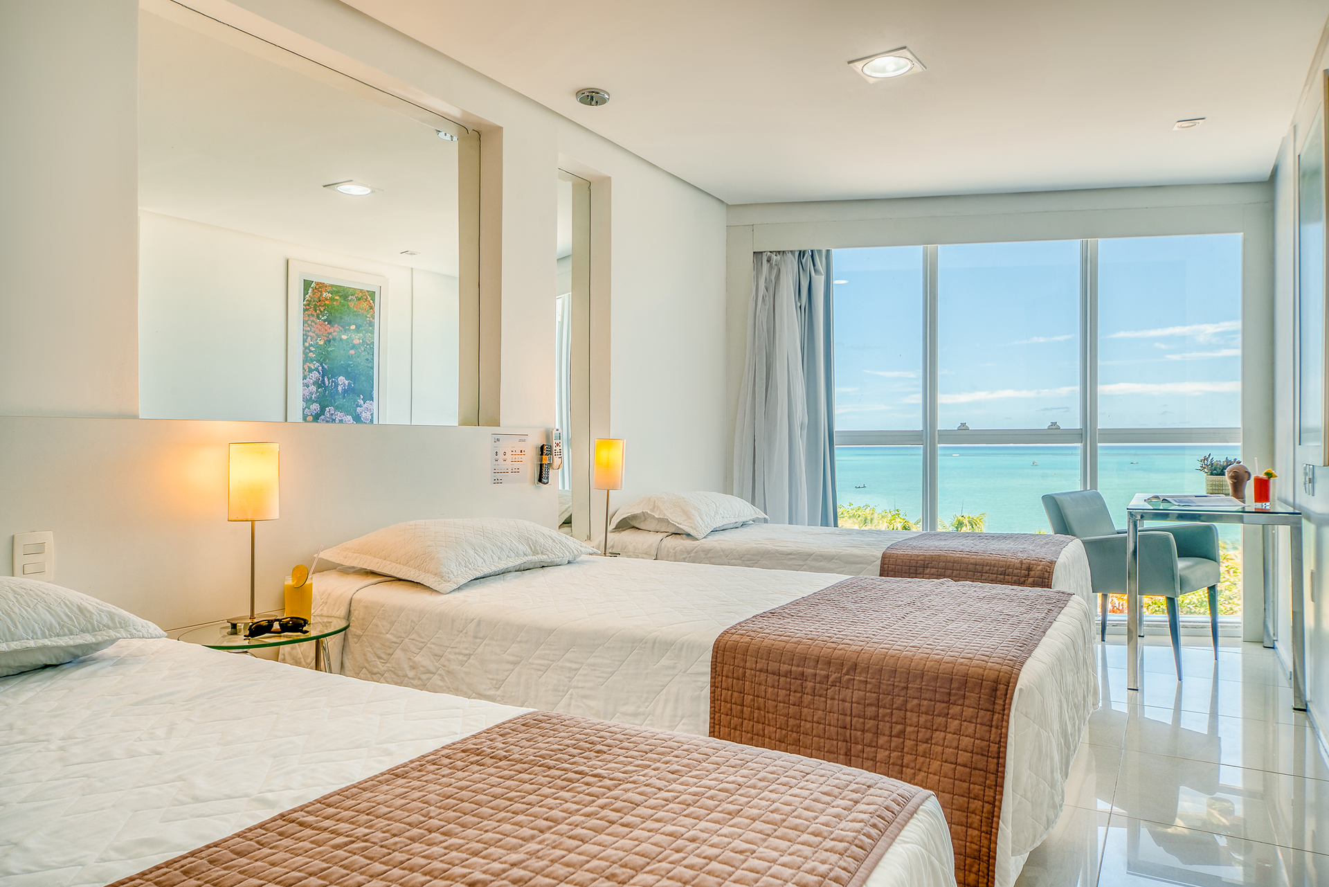 Resort à beira-mar com águas azul-turquesa, praia de areia, pessoas e edifícios sob um céu azul.