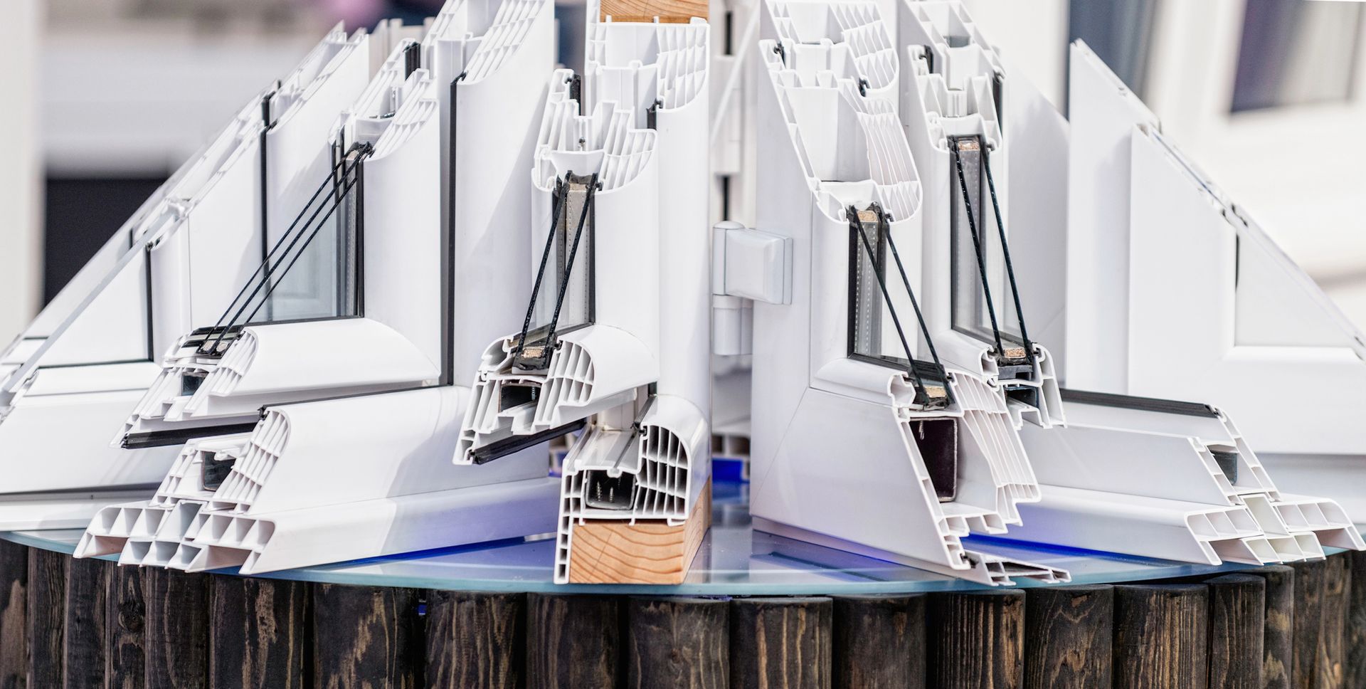 Vista in sezione di diversi profili per finestre in PVC bianco, esposti come campioni e posizionati su una base circolare in legno.