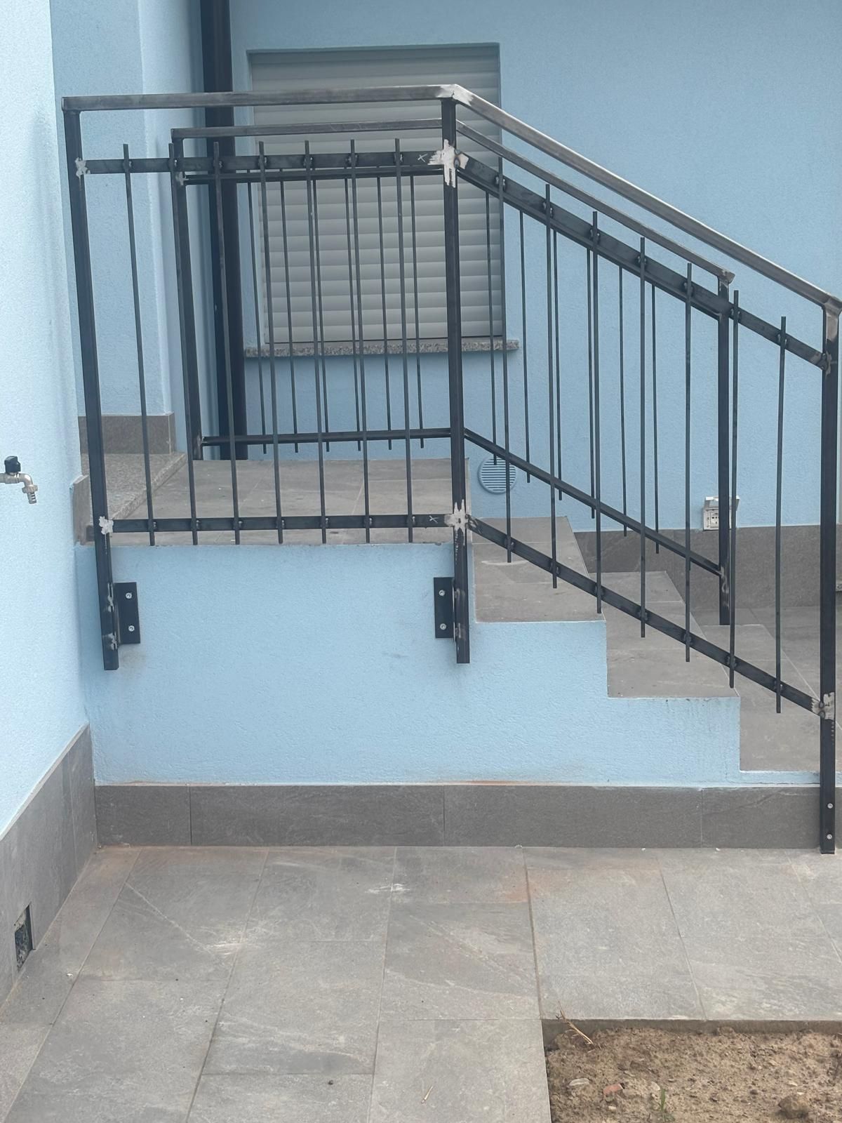 Ringhiera in metallo nero installata sui gradini in cemento che conducono alla facciata esterna di una casa azzurra.