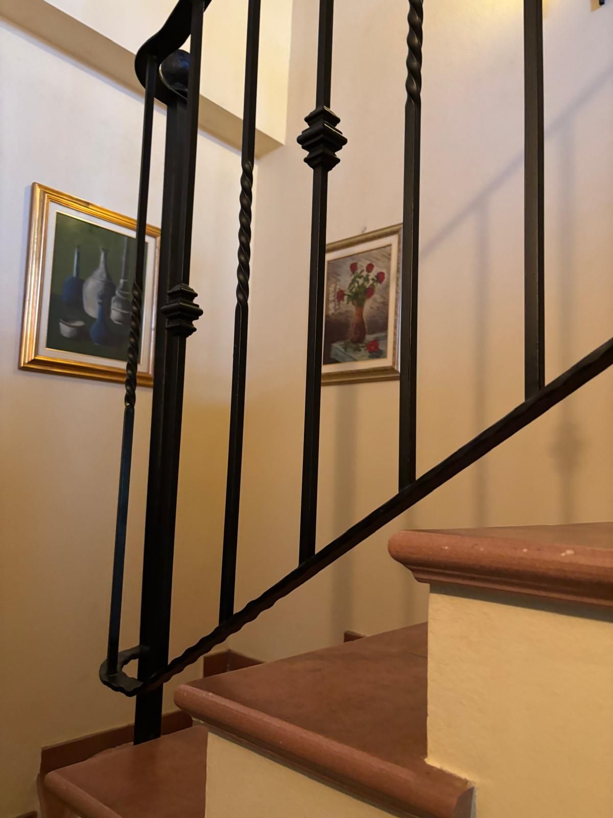 Una ringhiera in metallo scuro accanto alla scala, con due quadri incorniciati sulla parete chiara sullo sfondo.