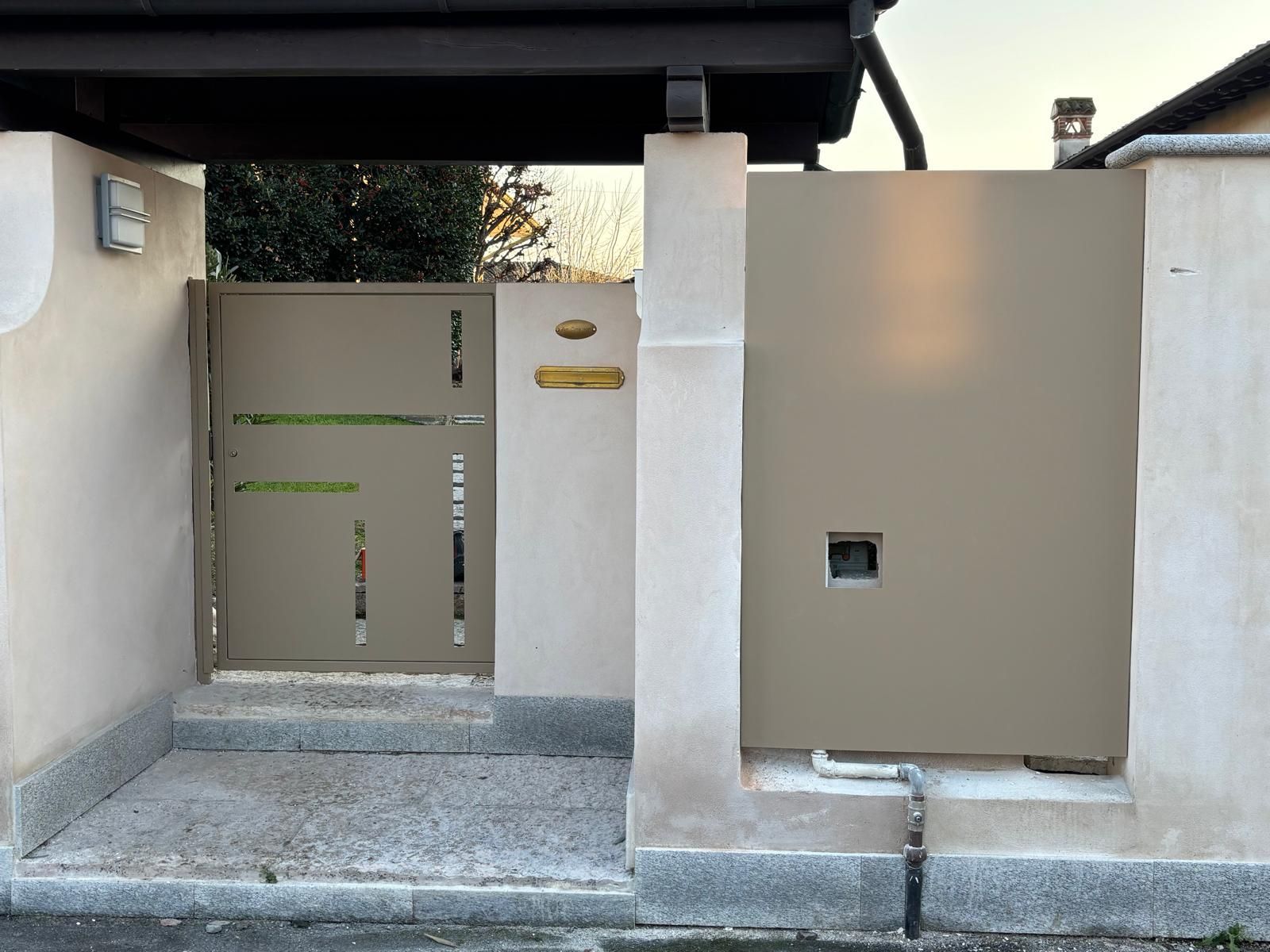 Un cancello pedonale beige accanto a un muro a pannelli beige su una base di pietra, protetto da una struttura sovrastante di colore marrone scuro.