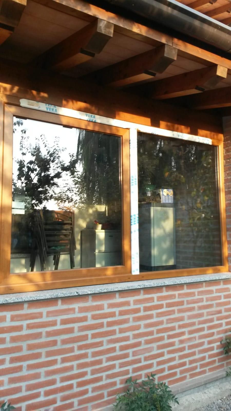 Una finestra con telaio in legno incastonata in un muro di mattoni, caratterizzata da un divisorio centrale verticale bianco con strisce di pellicola protettiva.