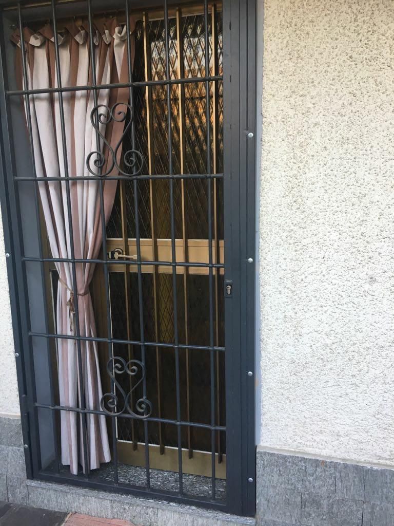 Un cancello di sicurezza in metallo nero installato sopra una porta, con una tenda beige appesa all'interno.