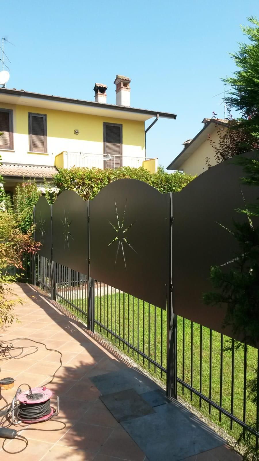 In un giardino residenziale, lungo una recinzione metallica nera, è installato uno schermo frangivista in metallo scuro e curvo con aperture a forma di stella.