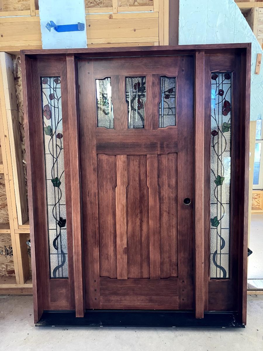 A wooden door with stained glass windows is sitting in a building under construction.