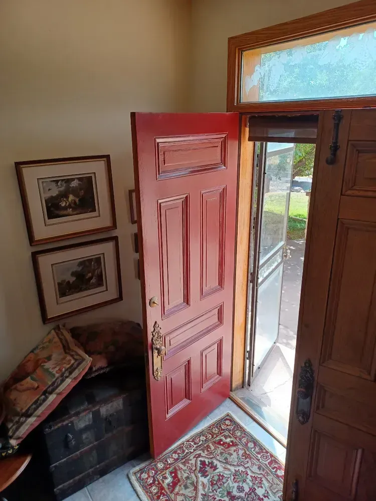 A red door is open in a room with pictures on the wall.