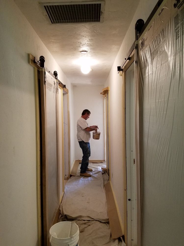 A man is painting a hallway with sliding barn doors.