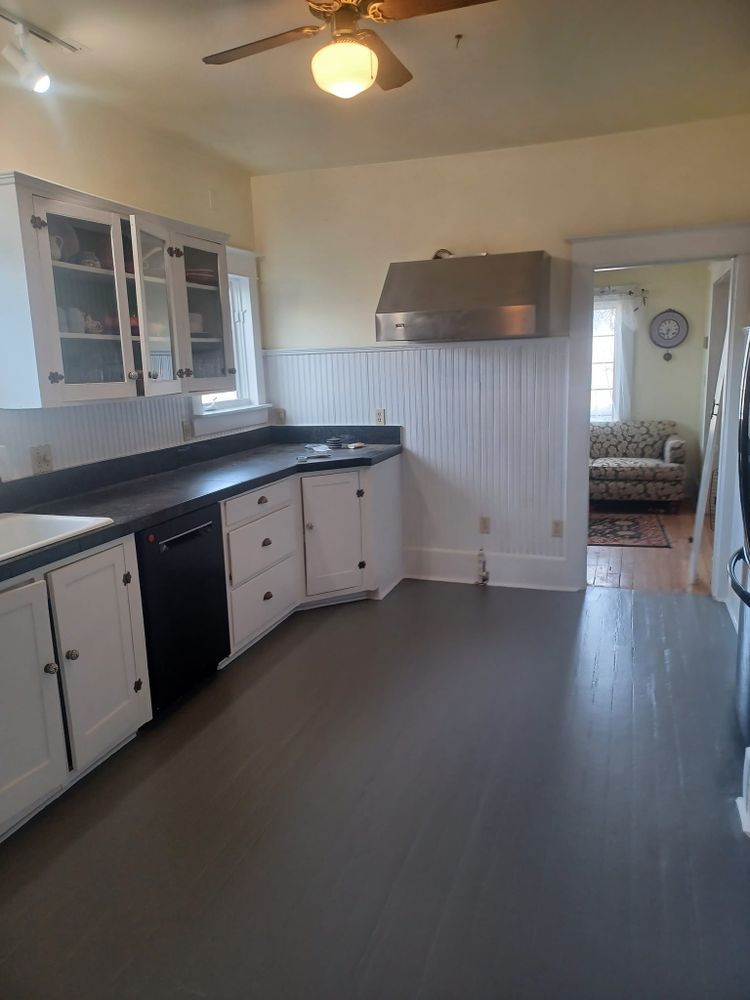 A kitchen with white cabinets , black appliances , and a ceiling fan.