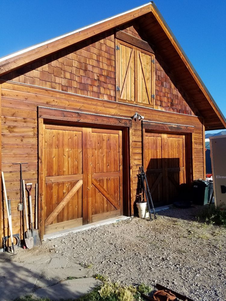 A wooden garage with two garage doors and a roof.