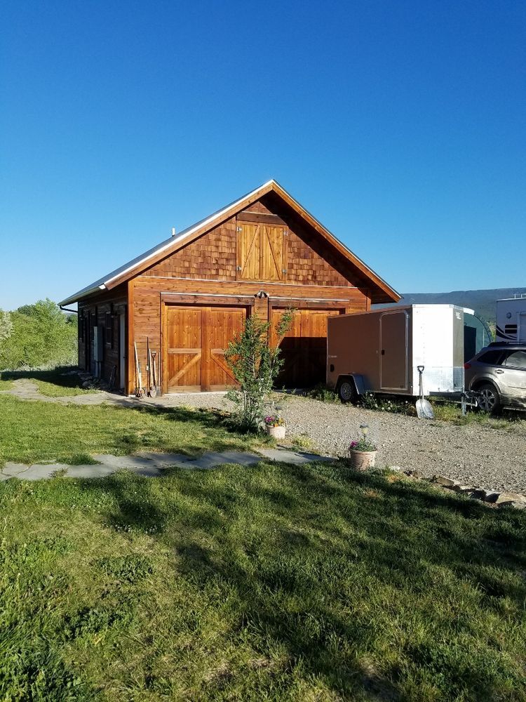 A large wooden barn with a trailer parked in front of it.