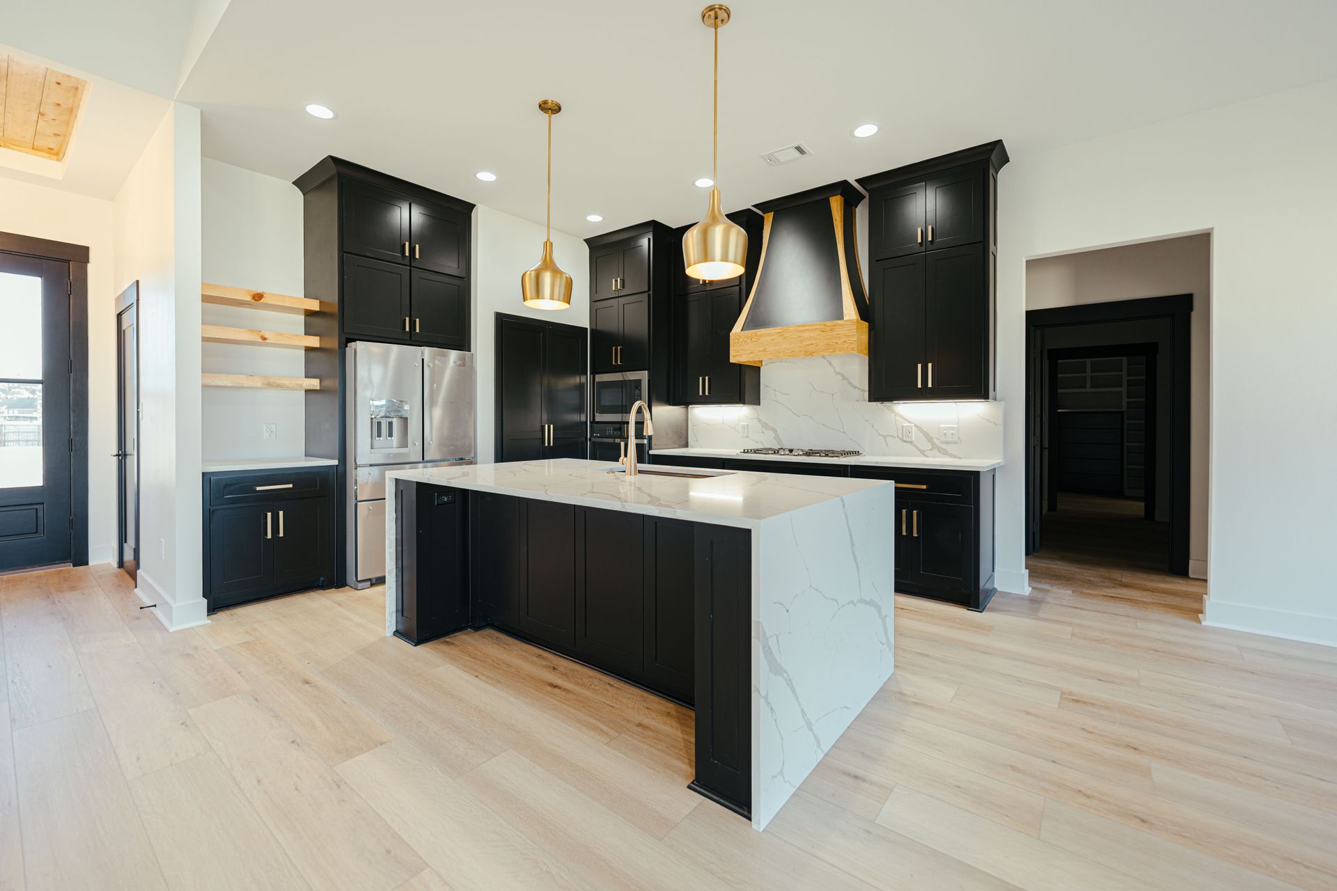 Contemporary kitchen with black cabinets, a marble island, and gold pendant lighting.