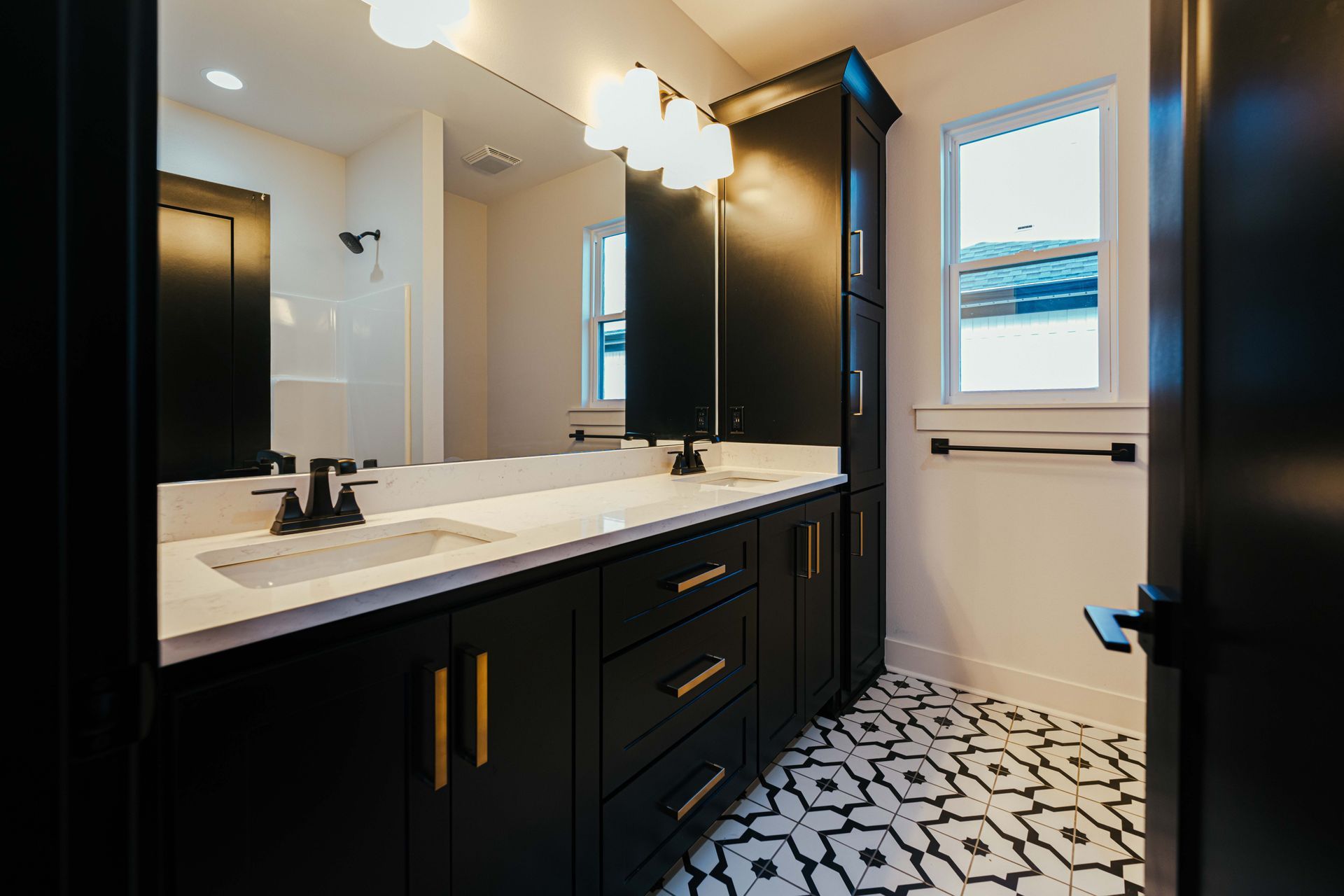 Stylish bathroom with double sinks, black cabinetry, and patterned floor tiles.