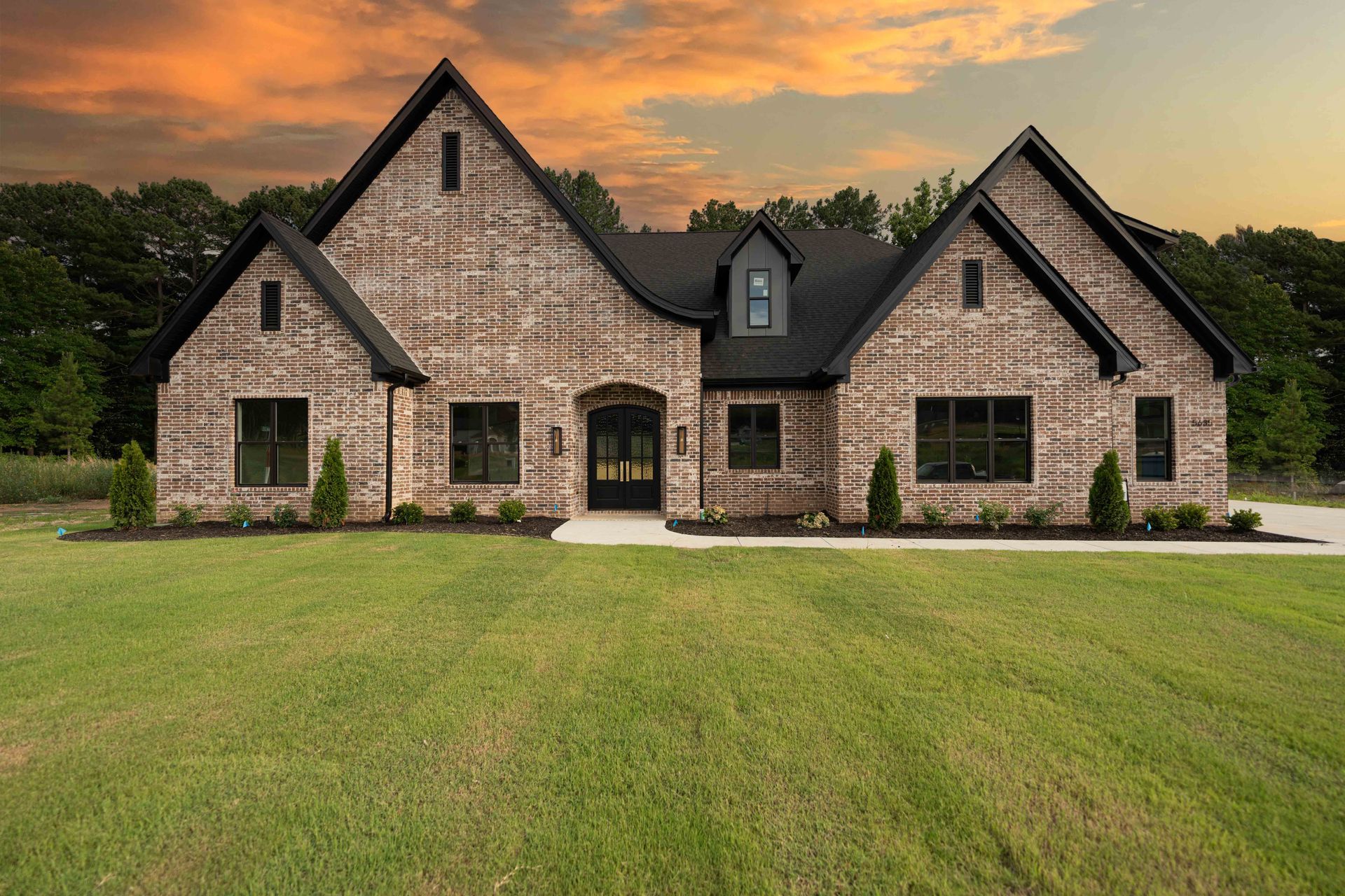 Large brick home with manicured lawn and a sunset in the background.
