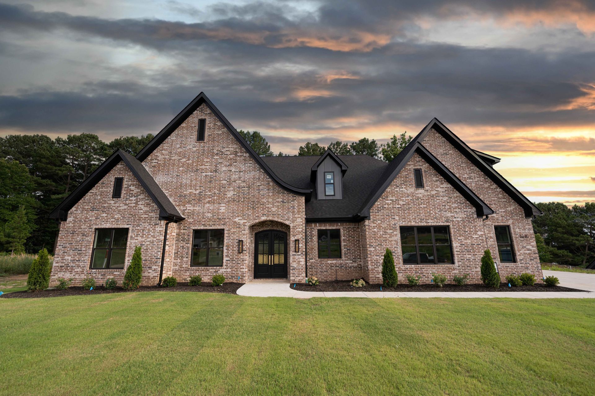 Stunning front exterior of a brick home with a large lawn and sunset view.