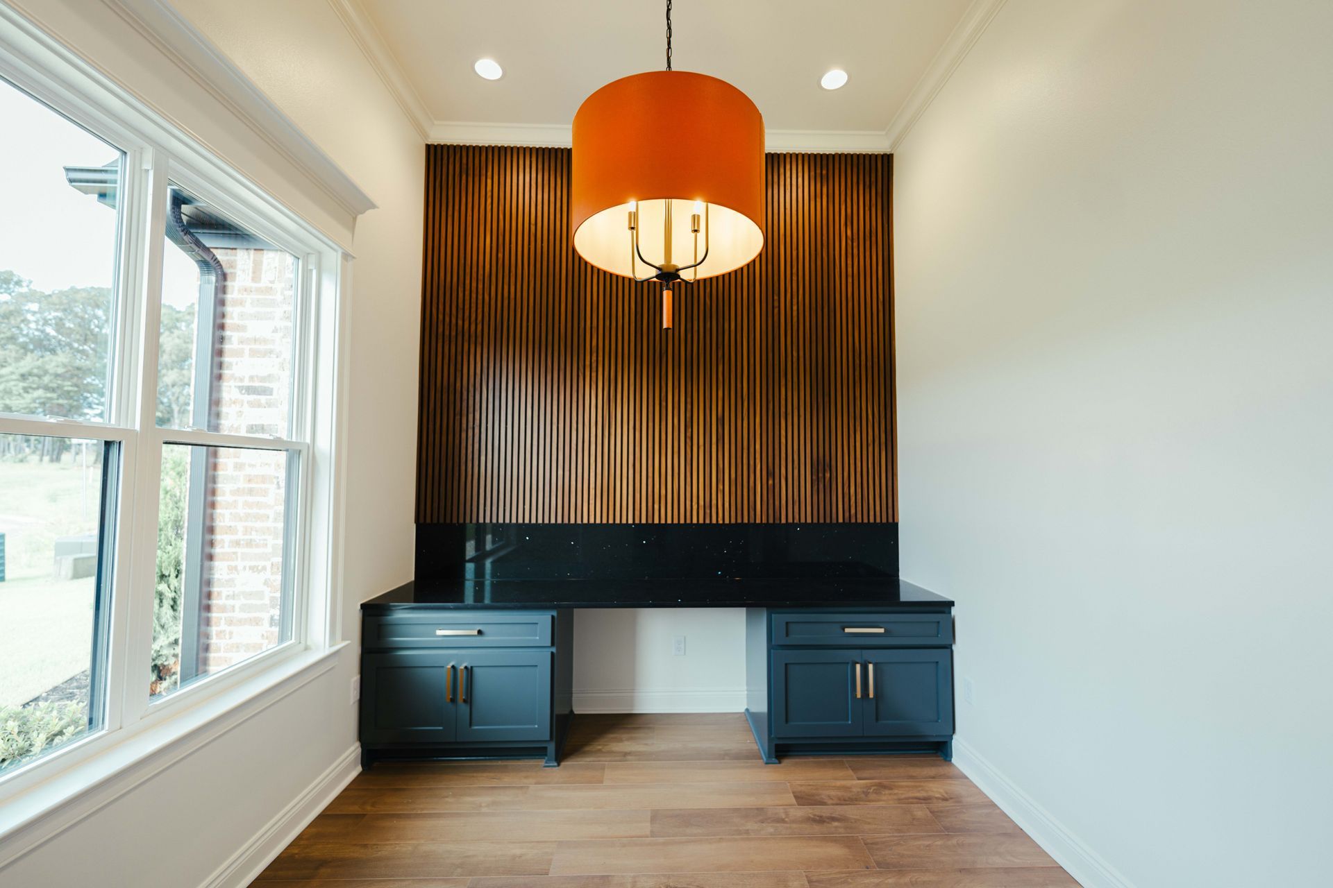 Home office with modern wooden accent wall, large window, and built-in desk.