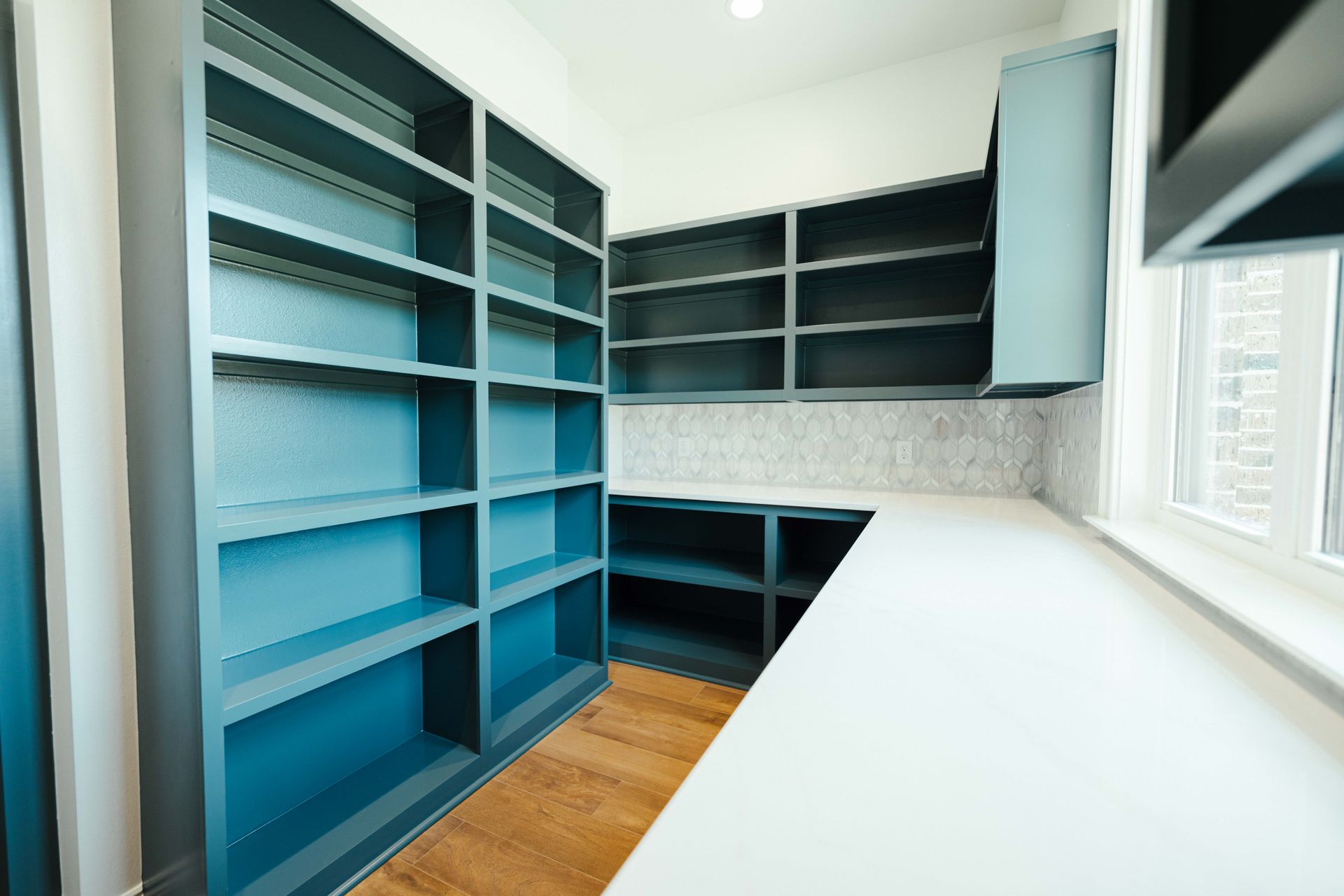 A walk-in pantry with teal shelving and a white countertop, providing ample storage space and custom organization.