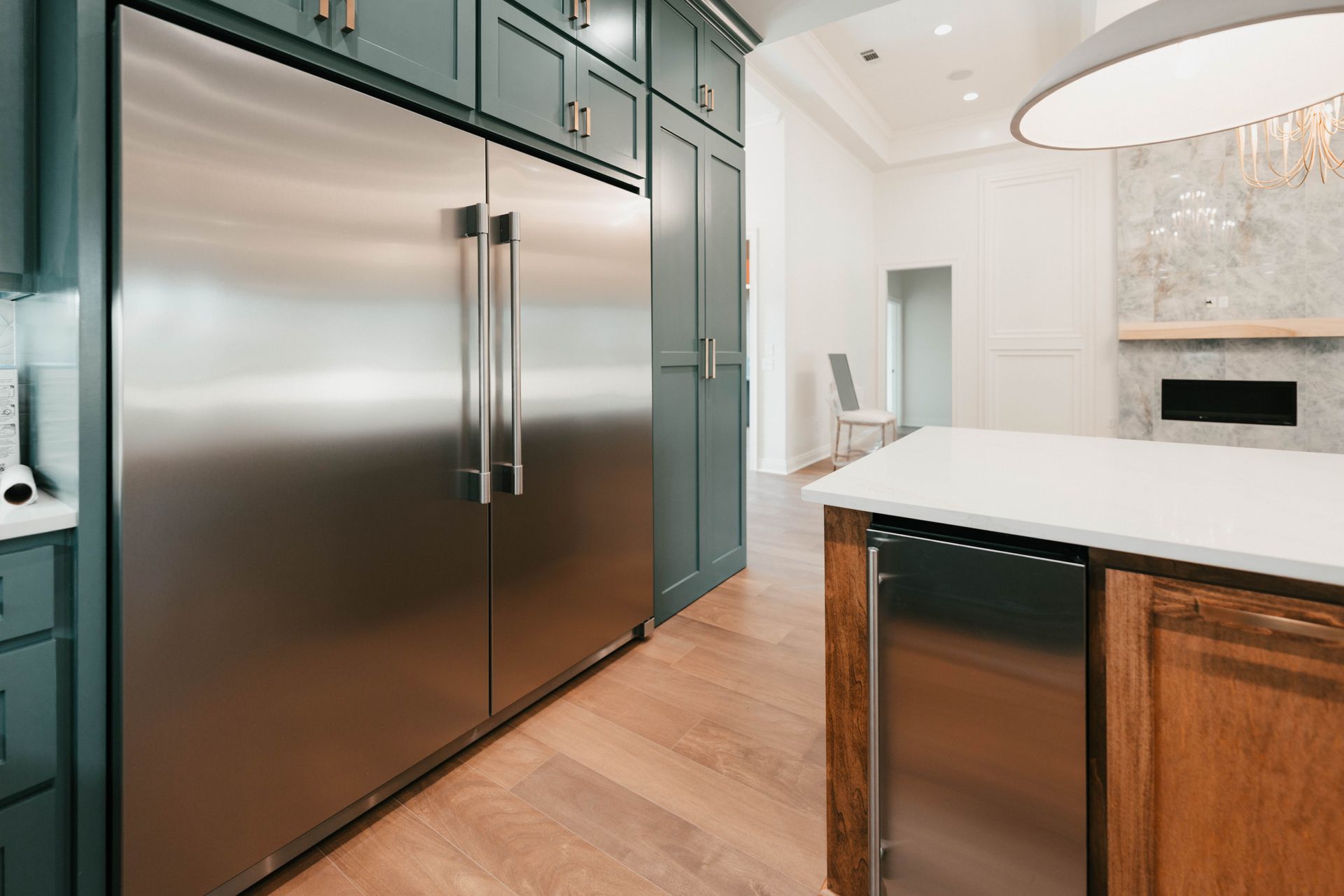 A close-up view of a sleek kitchen with stainless steel refrigerator, wooden floors, and modern cabinetry.