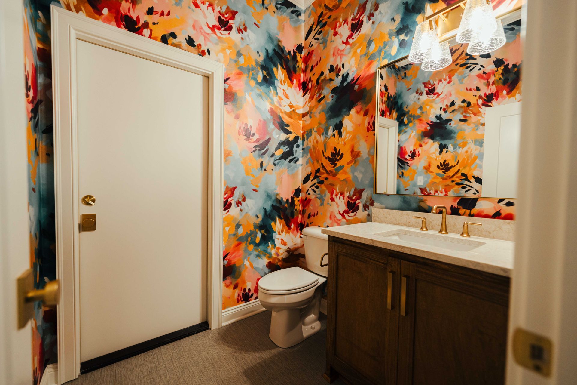 A vibrant half bathroom with colorful floral wallpaper, a wood vanity, and modern light fixtures.