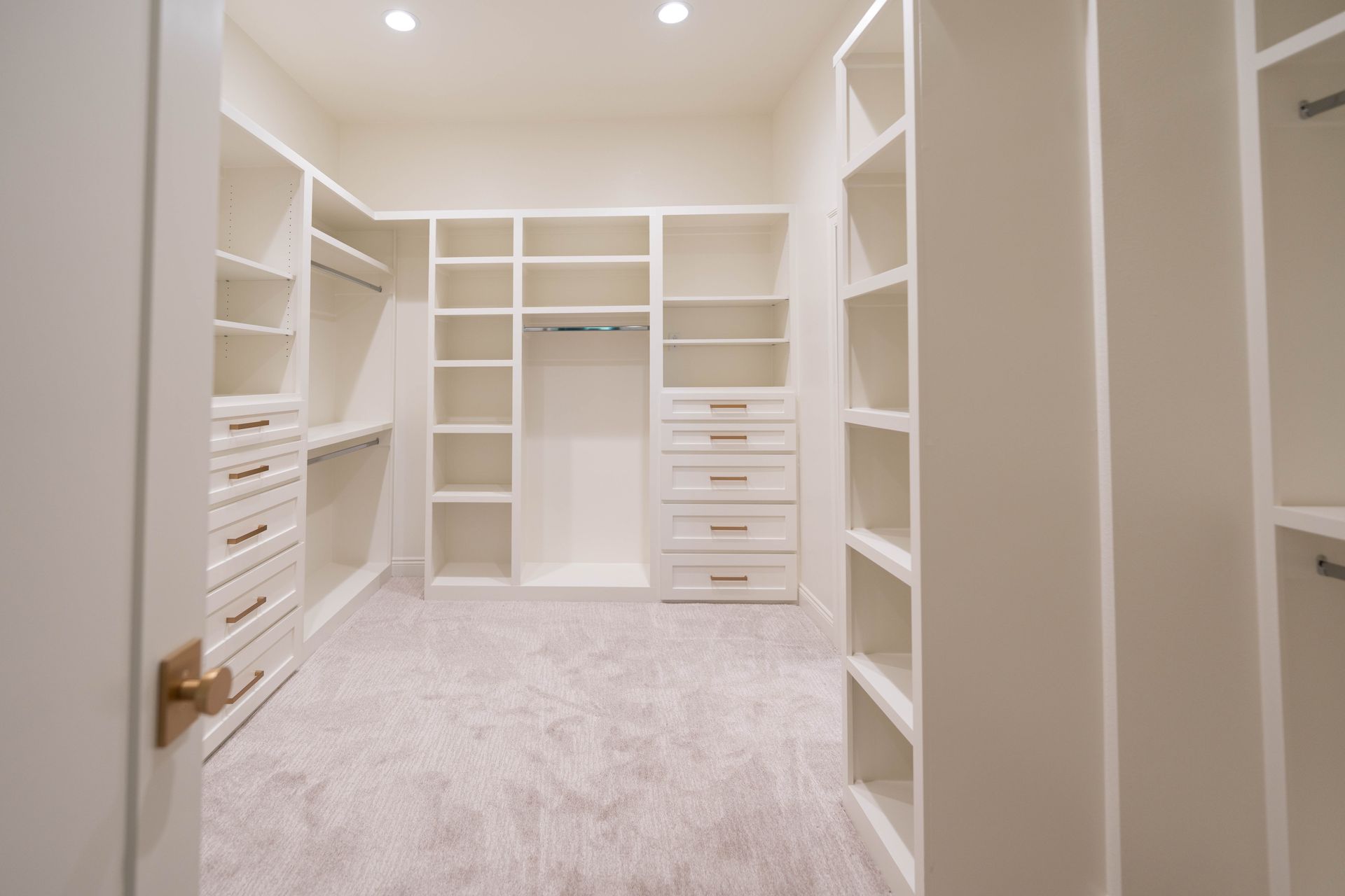 A spacious walk-in closet with white shelving, drawers, and hanging space for clothes, featuring soft carpeting.