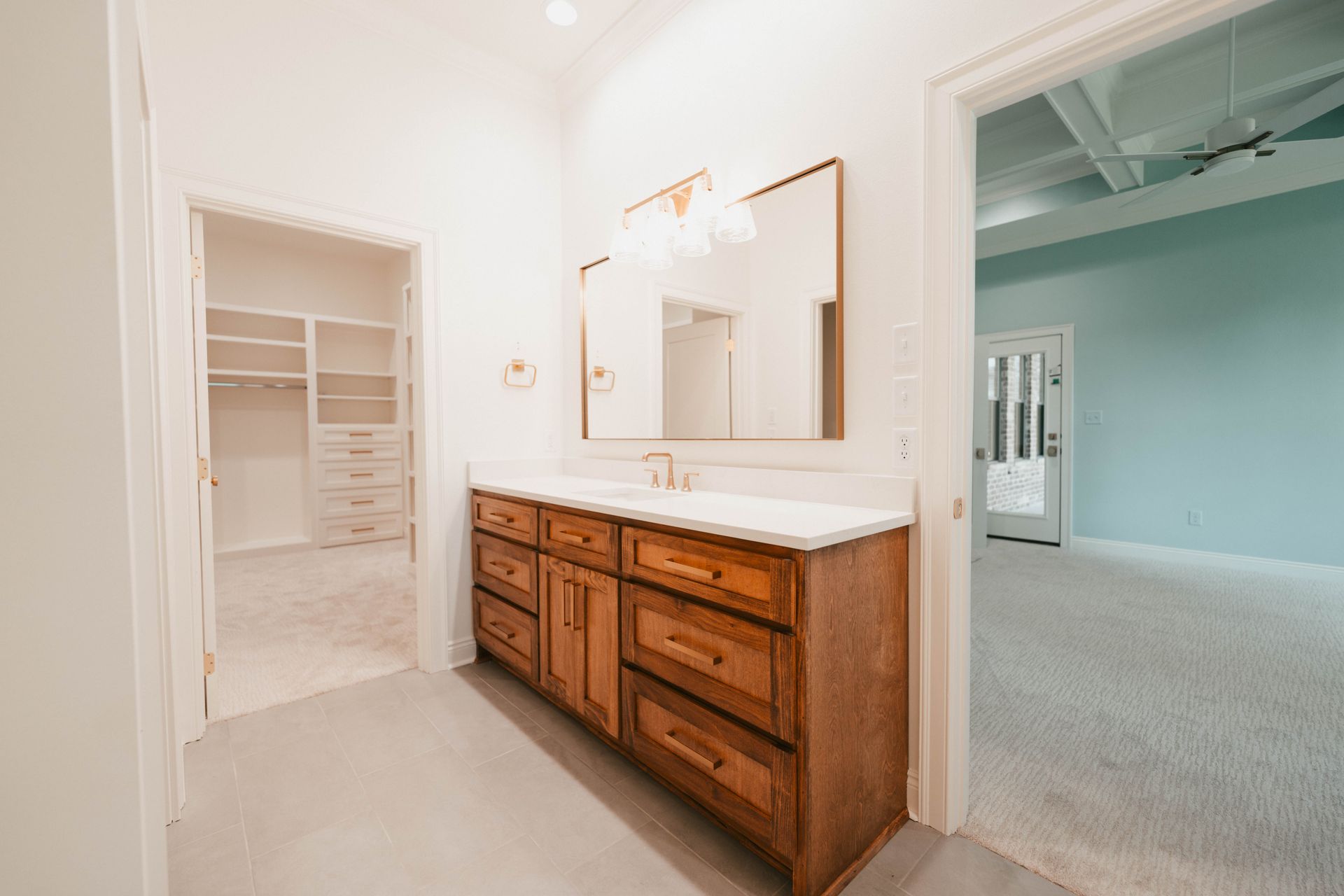 A spacious bathroom with a double vanity and wooden cabinets, leading to a walk-in closet.