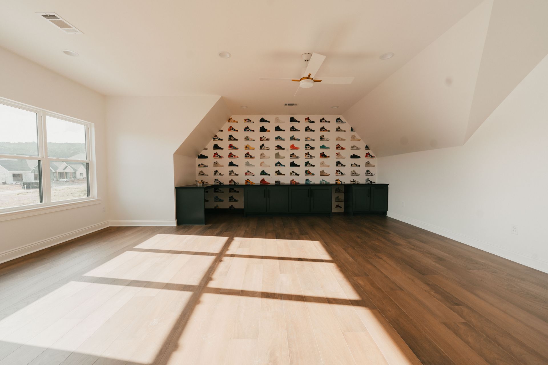 A large, well-lit bonus room featuring wood floors and a sneaker wallpaper accent wall