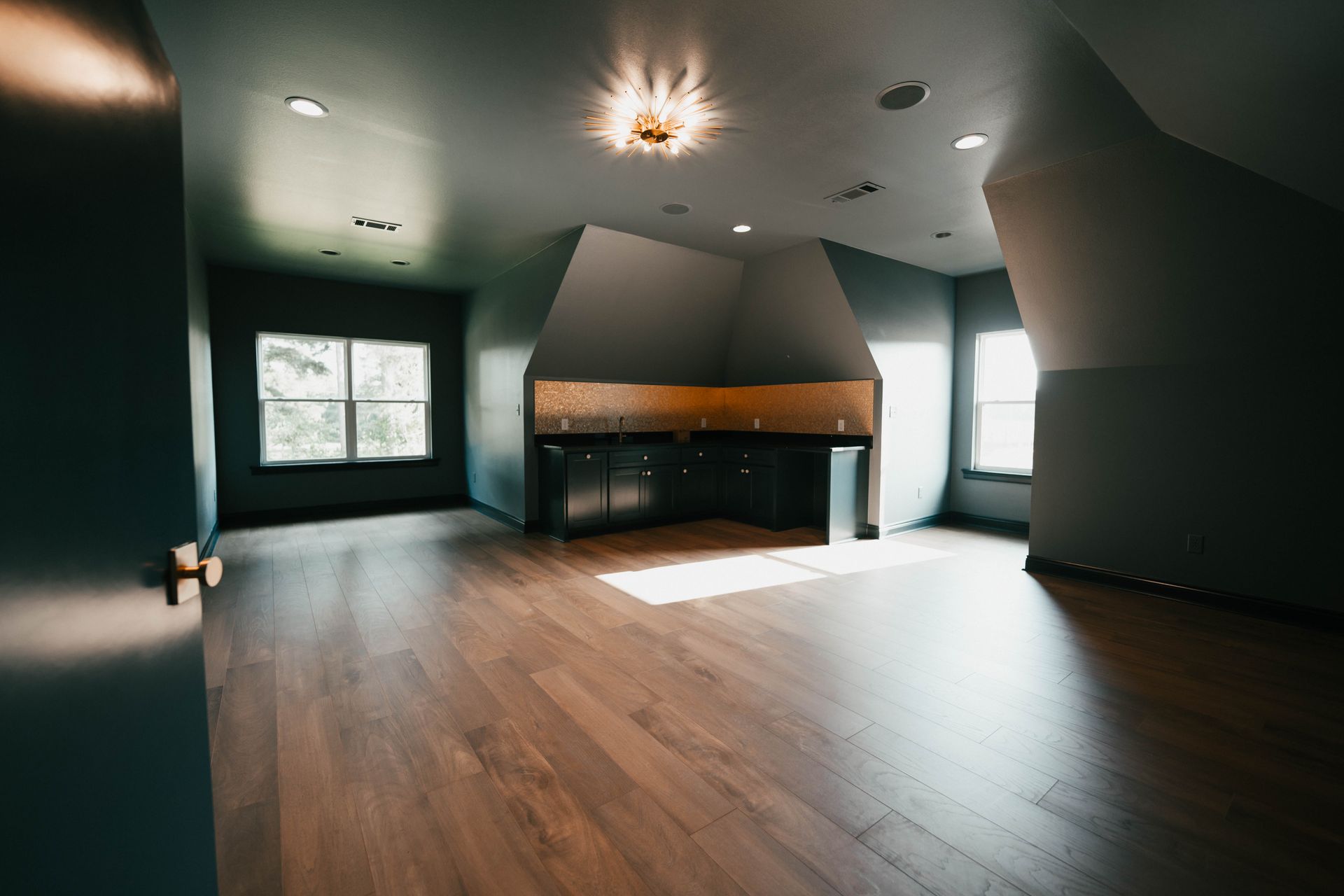 A dark-themed bonus room with built-in cabinets and natural lighting from windows.