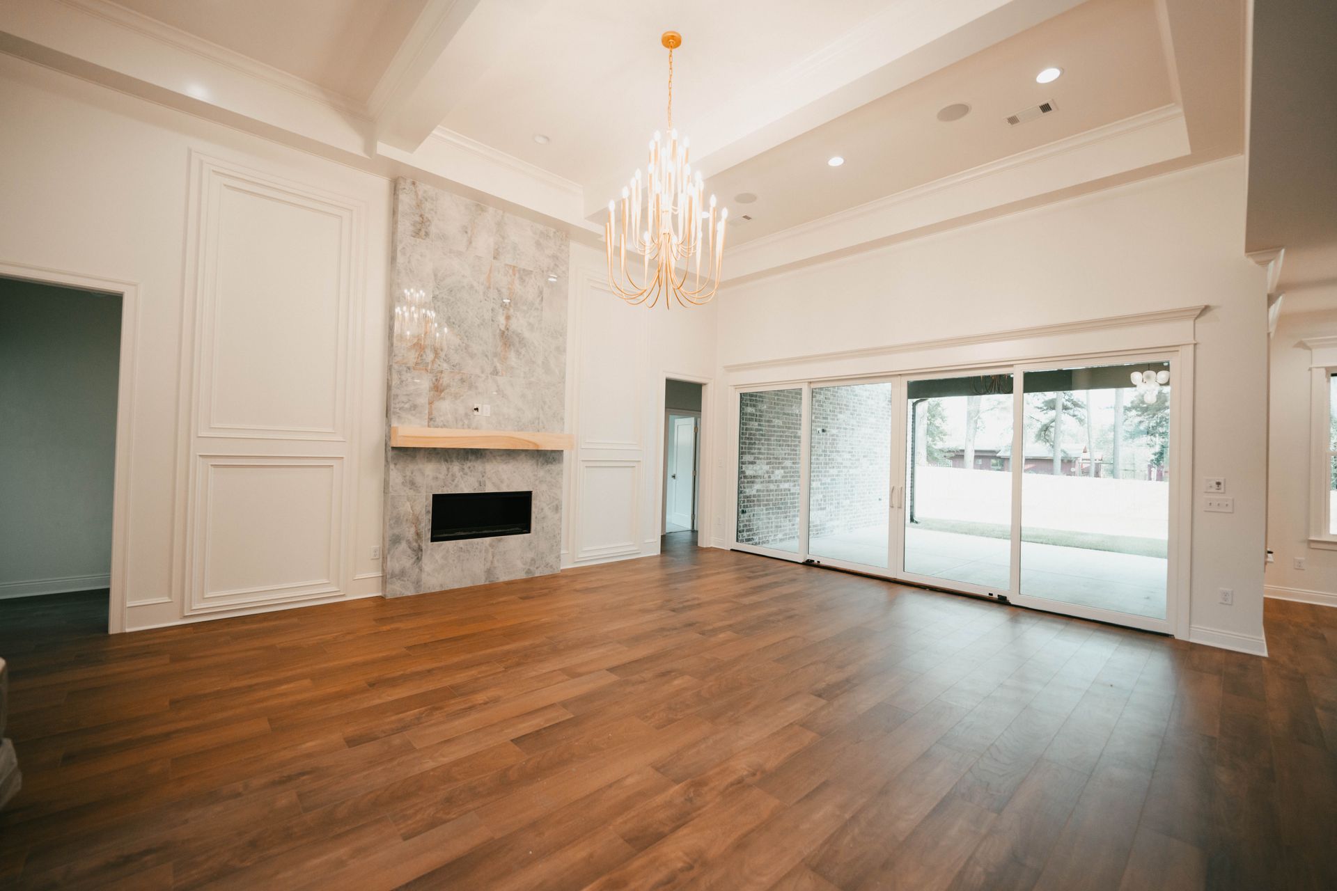 A modern living room with a large fireplace and hardwood floors, opening to a patio through sliding glass doors.