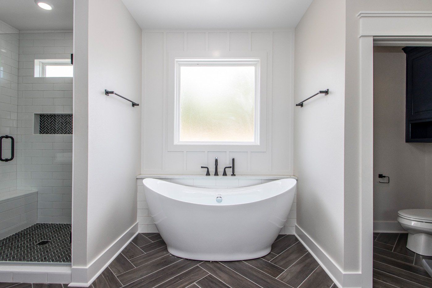 White standalone bathtub against a tiled wall, located in a bright, modern bathroom.