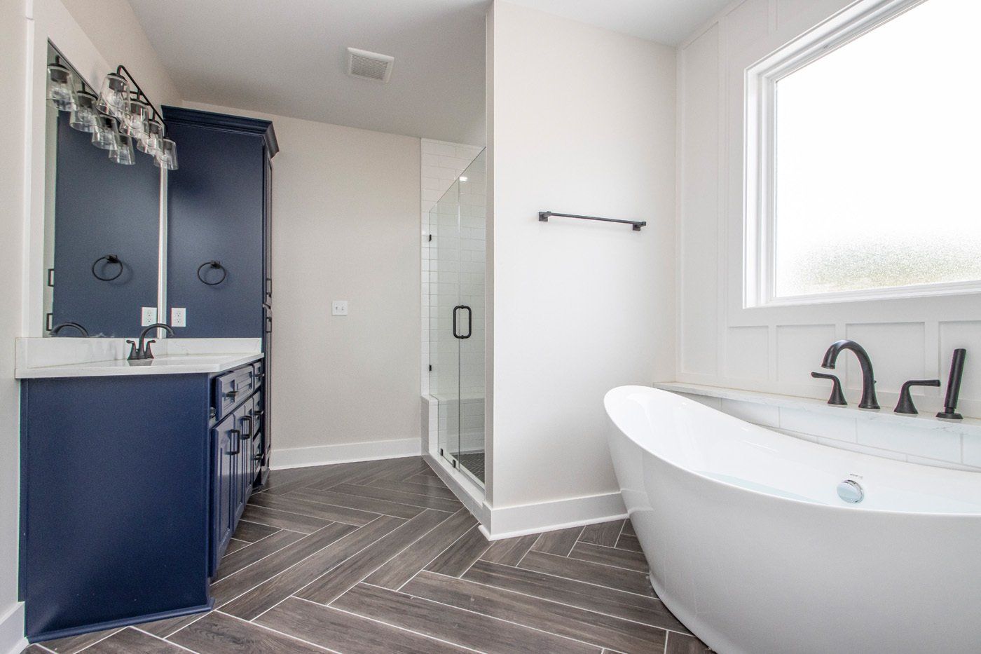 Blue and white bathroom featuring a freestanding tub, large vanity with mirrors, and modern shower.