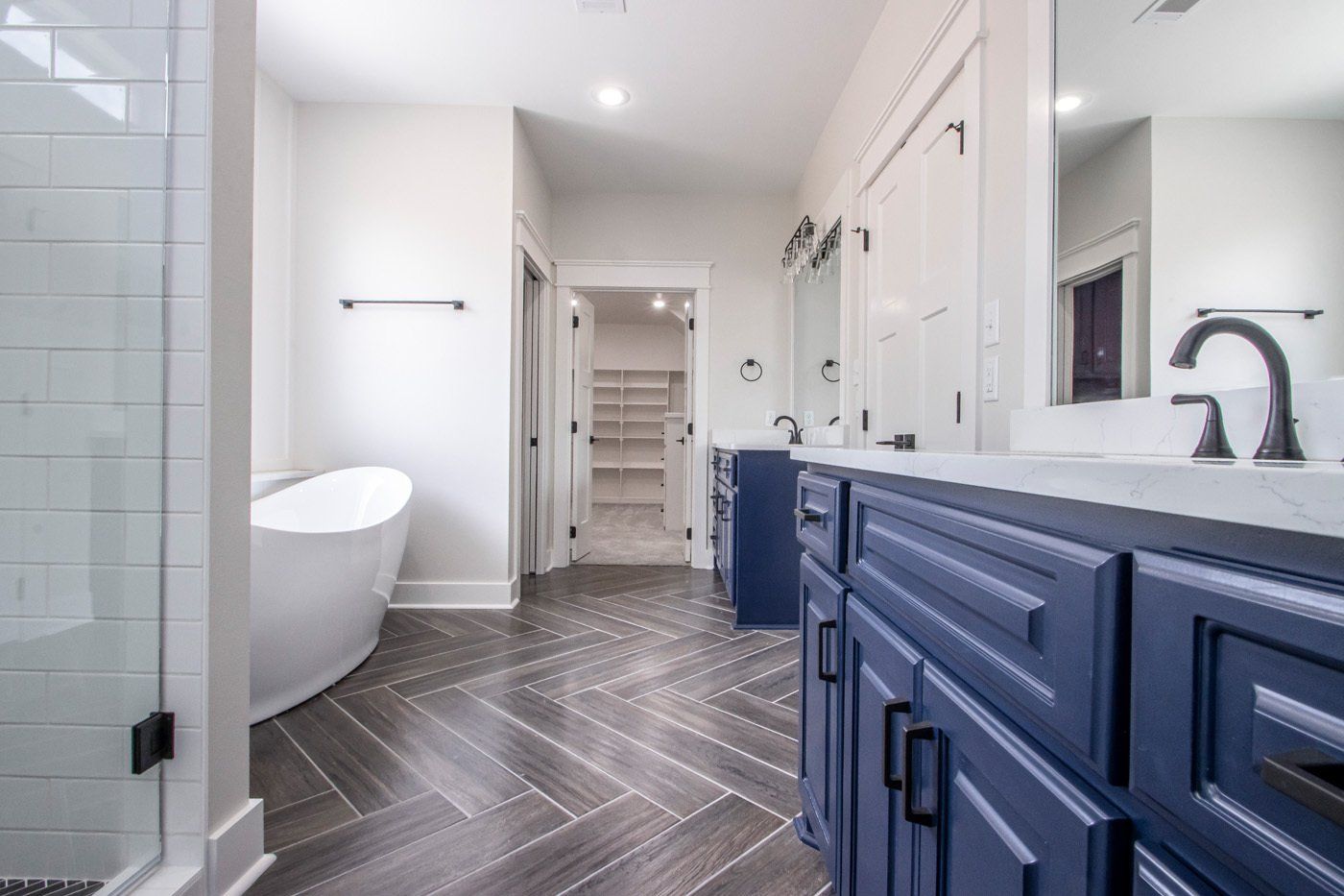 Spacious bathroom with a navy double vanity, white tub, and modern tile flooring.