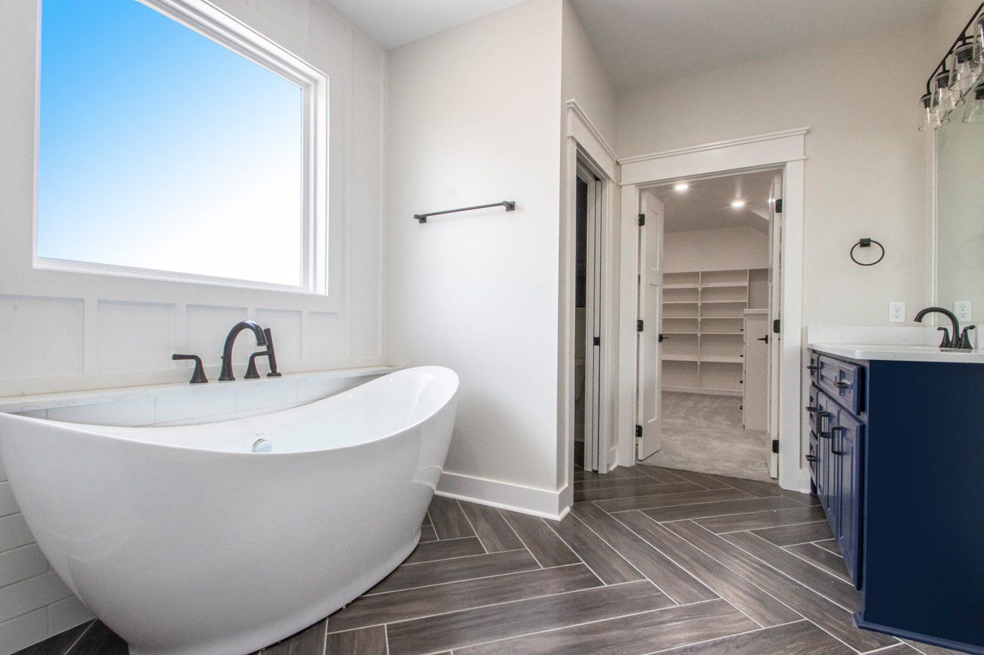 Modern bathroom with a standalone tub, navy vanity, and tile flooring leading into a walk-in closet.