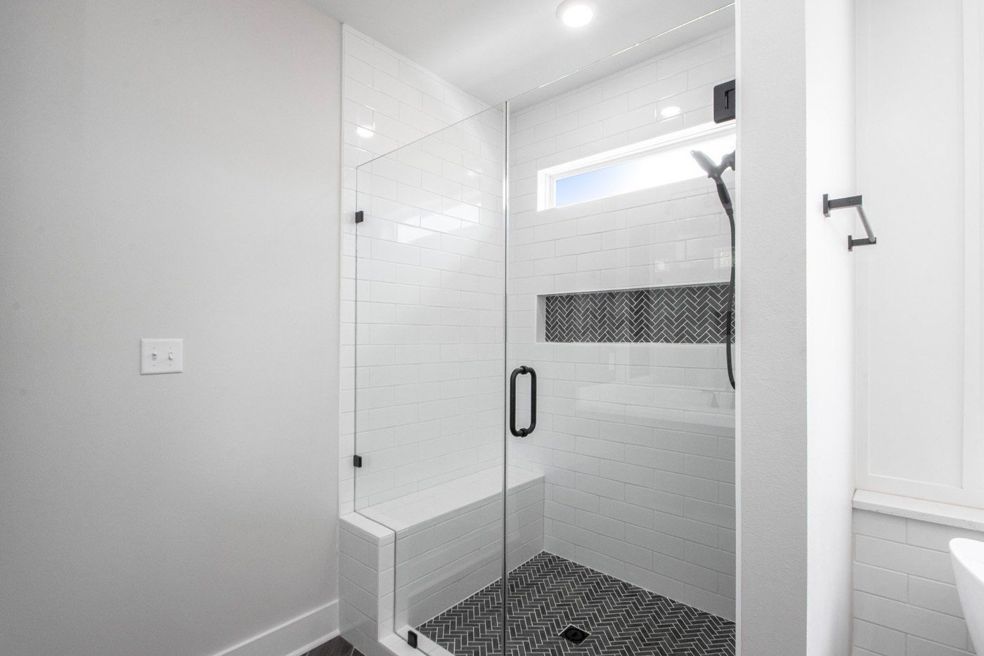 Modern bathroom with a walk-in shower, white tile, and black accents.