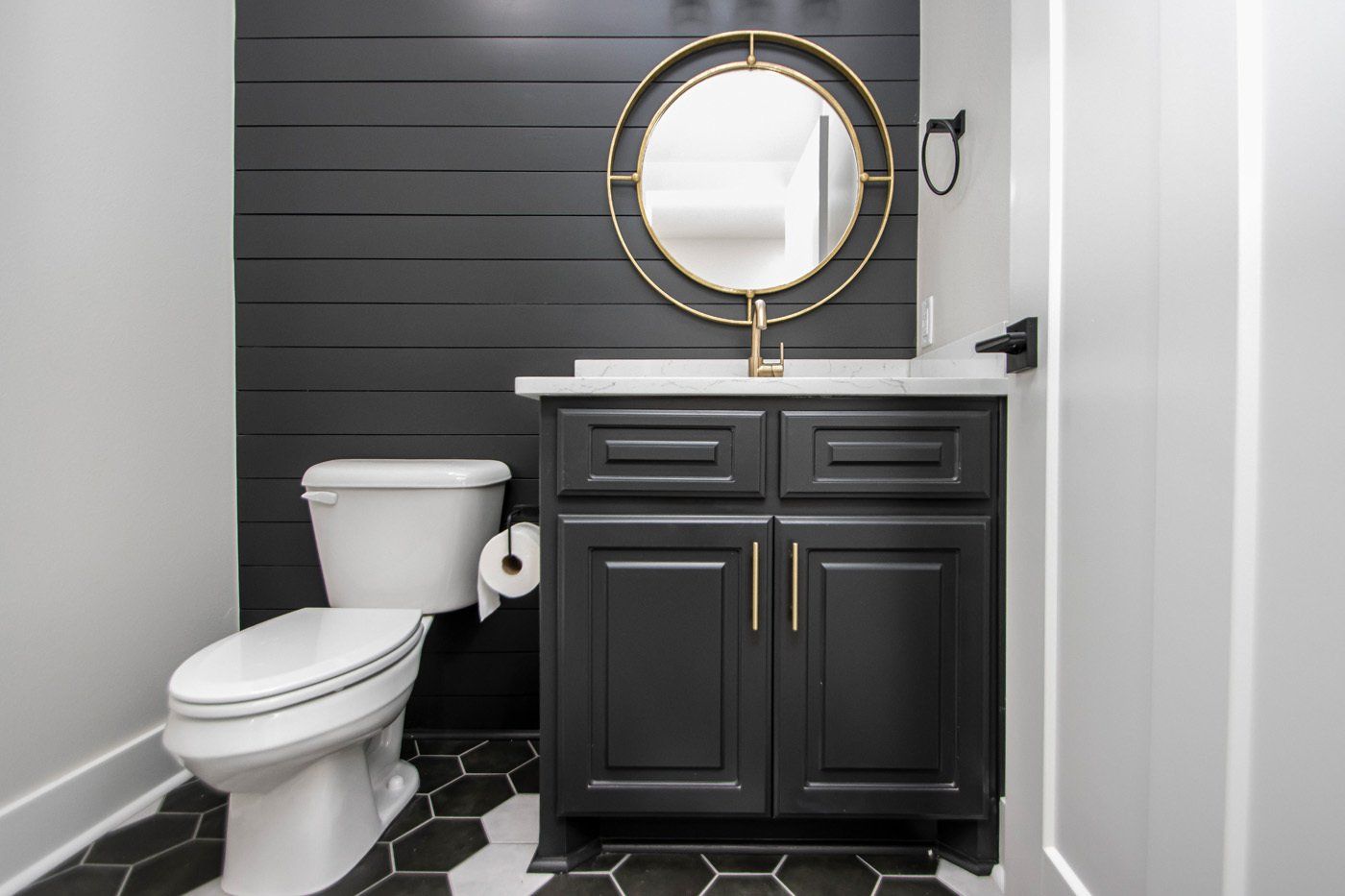 Modern half-bath with a black vanity and a round gold mirror.