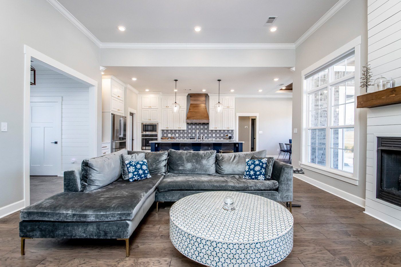 A spacious, elegant living room with a gray couch, fireplace, and large windows offering natural light.