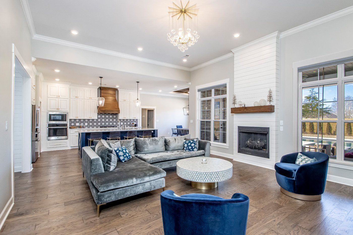 Spacious living room with a velvet couch set and modern kitchen in the background.