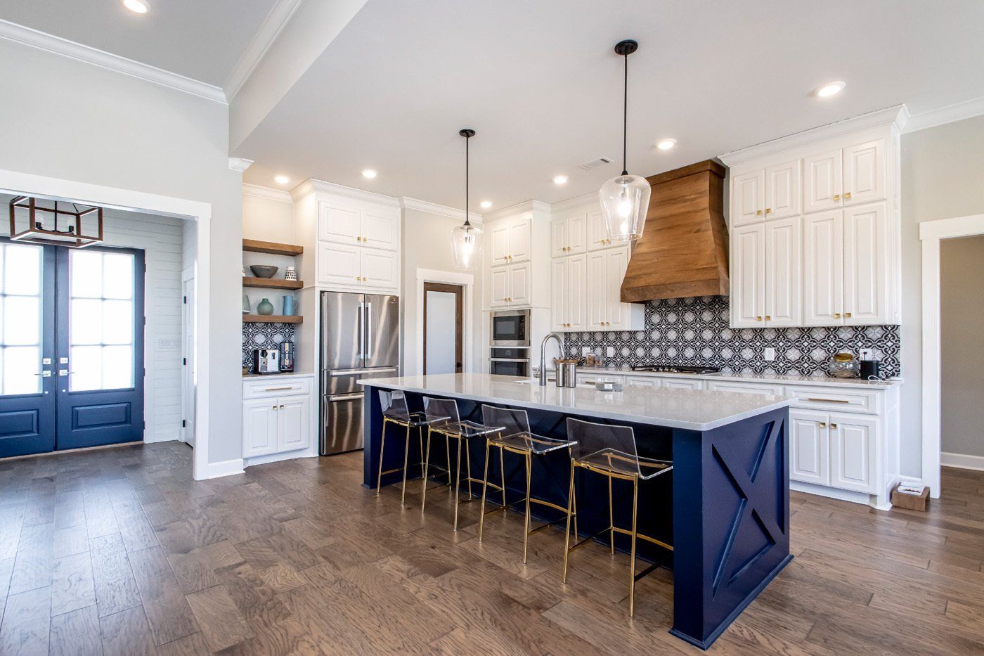 A modern kitchen featuring white cabinetry, dark blue island, and wooden range hood and stainless steel appliances.