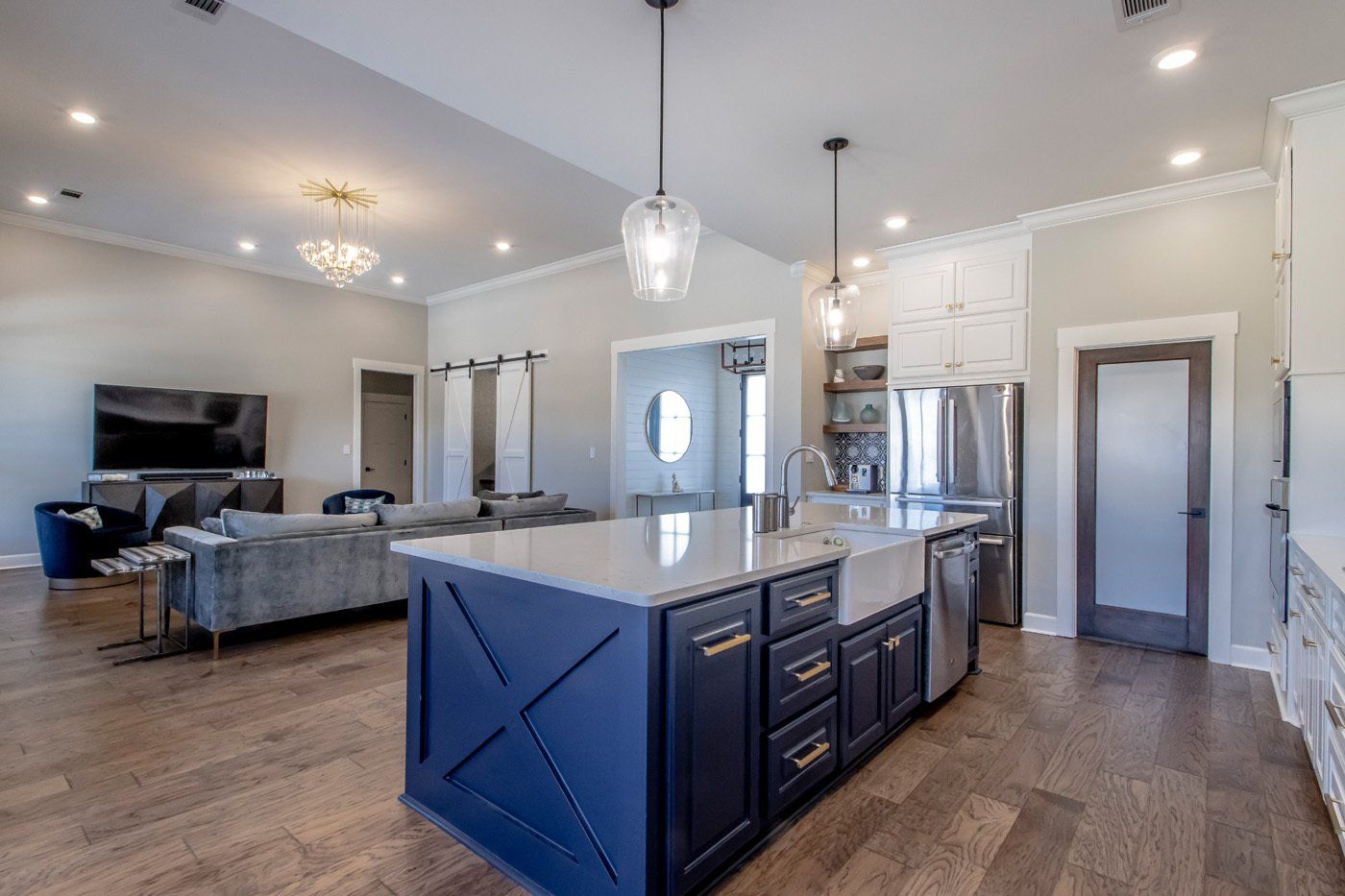 Open kitchen and living area with a navy island, white cabinets, and wood flooring leading to a cozy living room.
