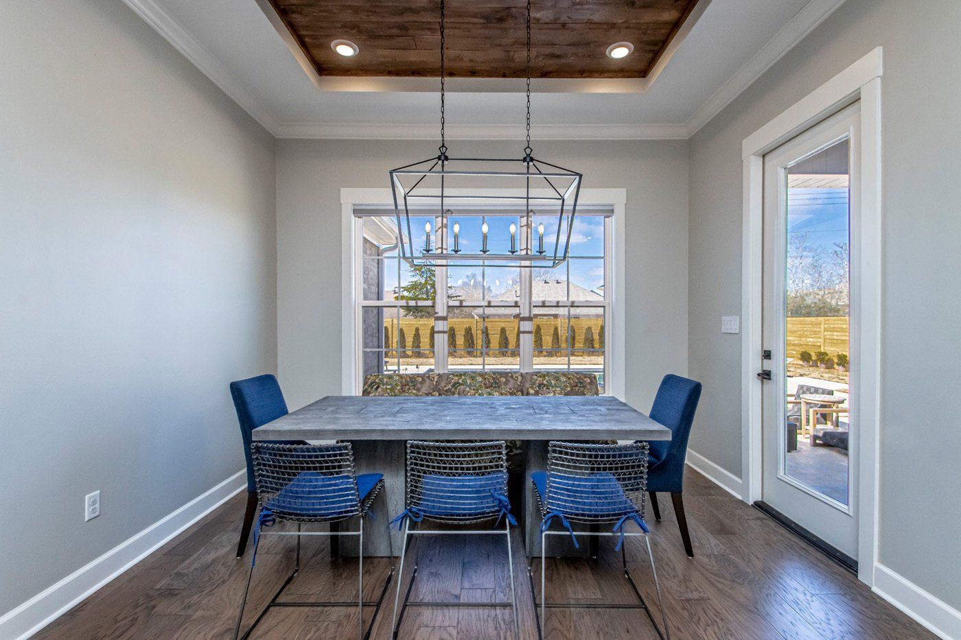 A bright dining area featuring a modern rectangular light fixture, dark wood table, and blue chairs, with large windows