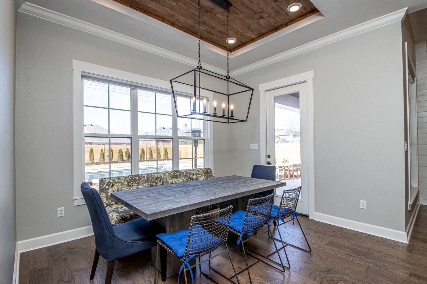 Bright dining room with a wood table, blue chairs, and a modern light fixture beneath a wood-paneled ceiling.
